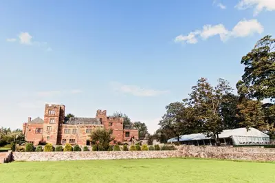 an old castle with a stone wall and a grass field at Dalston Hall in Carlisle