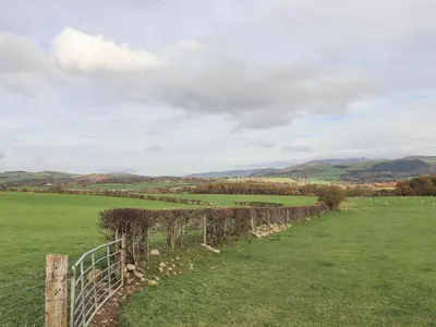 a fence in a field with sheep in the distance at Tithe Cottage in Cockermouth
