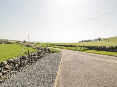 a road with a stone wall next to a field at Longforth Farm Cottage in Gillespie