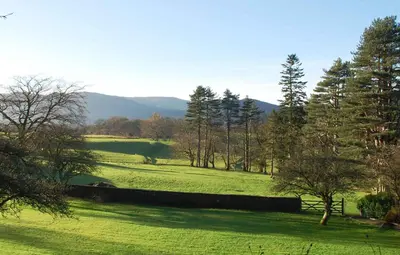 a green field with trees and mountains in the background at Ravenstone Lodge Country House Hotel in Keswick