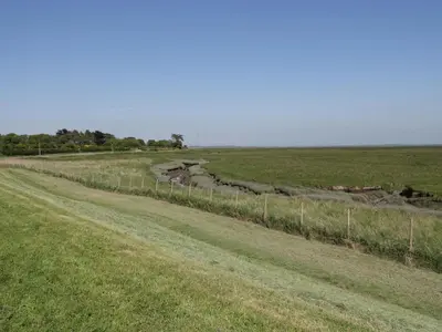 a dirt road in a field with a fence at Marsh Villa in Skinburness