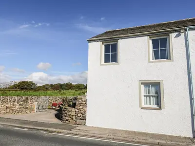 a white house with a stone wall next to a street at 1 Park Nook Close in Waberthwaite