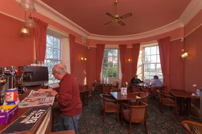 an older man standing at a table in a restaurant at Woodland House Hotel in Dumfries