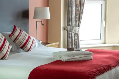 a bedroom with a white bed with a red blanket and a window at Ellan Vannin Hotel in Douglas