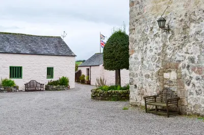 a bench sitting next to a building with a flag at The Lady Maxwell Room at Buittle Castle in Dalbeattie
