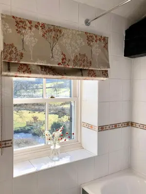 a bathroom with a window with a curtain and a vase with flowers at Kirkstile Inn in Loweswater