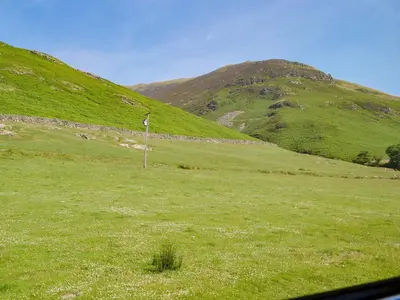 a field of green grass with a mountain in the background at Brackendale Cottage - Uk1335 in Threlkeld