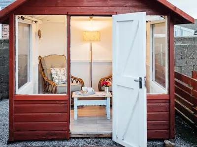 a red shed with a door open with a chair and a table at The Bothy - Uk5803 in Girthon