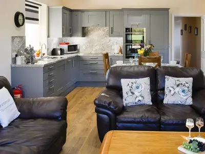 a living room with two leather couches and a kitchen at Liftingstane Dairy Cottage in Closeburn