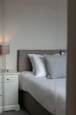 a bed with white pillows and a night stand with a lamp at The Huntington - Donnini Apartments in Ayr