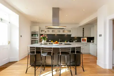 a kitchen with white cabinets and a large island with bar stools at Sea Breeze - Donnini Apartments in Ayr