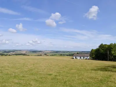 a large field of grass with a house in the distance at Brae Cottage in Kelton
