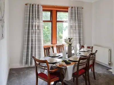 a dining room with a table with chairs and a window at Brae Cottage in Kelton