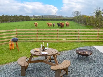 a picnic table and chairs with cows in a field at Greengill Farm Shepherds Hut- Ukc3632 in Gilcrux