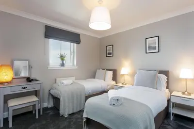 a bedroom with two beds and a desk and a window at Harris Retreat - Donnini Apartments in Ayr