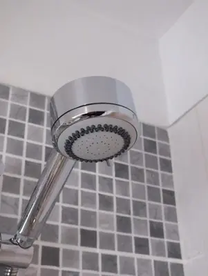 a shower head in a bathroom with gray tiles at Boggle Dyke Cottage in Thornhill