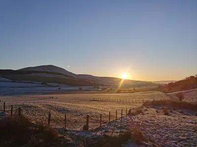 a sunset in a field with the sun setting at Glen Roe - 3 Bed Lodge on Friendly Farm Stay in New Cumnock