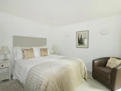 a white bedroom with a bed and a chair at Holemire Barn in Cockermouth