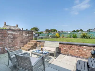 a patio with chairs and tables and a brick wall at Coney Garth Retreat in Beckermet