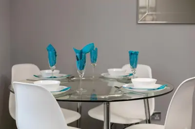 a dining room table with blue glasses and white chairs at Forbes Retreat - Donnini Apartments in Ayr