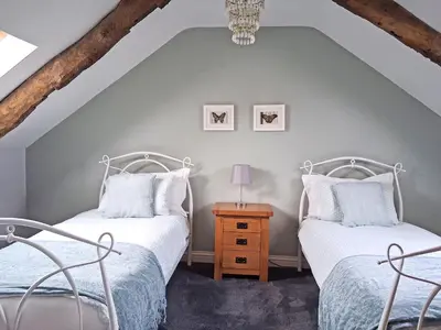 two beds in a attic bedroom with two chairs at Swallow Barn in Torpenhow