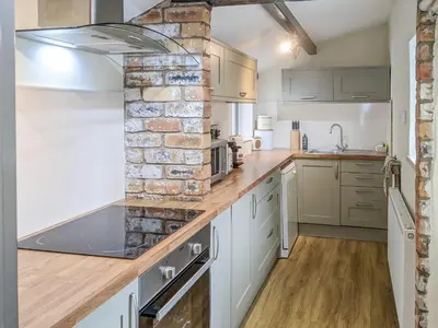 a kitchen with white cabinets and a brick wall at Seascape Cottage in Allonby