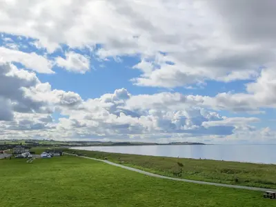 a grassy field next to a large body of water at Seascape Cottage in Allonby
