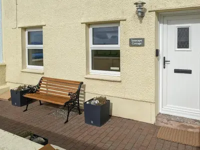 a wooden bench sitting outside of a building with a door at Seascape Cottage in Allonby