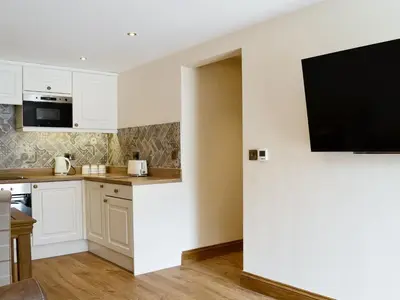 a kitchen with white cabinets and a flat screen tv at The Byres Tan in St Bees