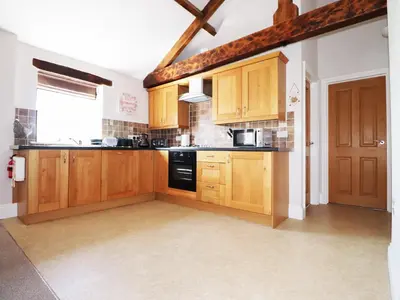 a large kitchen with wooden cabinets and a window at Carleton Mill Cottage in Carlisle