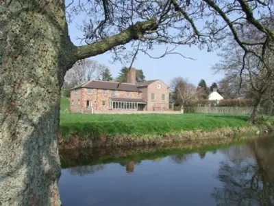 a large brick building next to a body of water at Carleton Mill Cottage in Carlisle