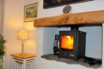 a wood burning stove in a room with a lamp at Romantic Quirky Cottage with private garden and parking in Beckermet