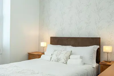a bedroom with a bed with white sheets and two lamps at Carlton 2 a large modern Keswick appt with parking in Keswick