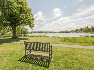 a park bench sitting in the grass near a lake at Garden Cottage in Castle Douglas