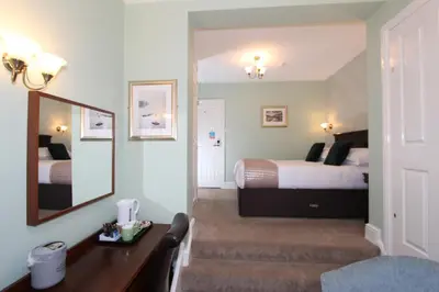 a bedroom with two beds and a desk and a mirror at Fern Howe Guest House in Keswick