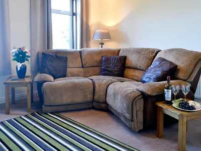 a brown couch in a living room with a table at Butterhole Cottage in Kelton