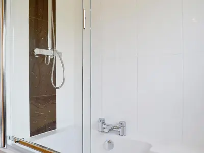 a shower with a glass door next to a sink at Ghillie Cottage in Cockermouth