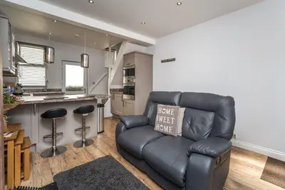 a living room with a leather couch and a kitchen at Isabel Cottage in Keswick