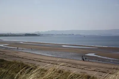 a beach with people walking on the sand and the water at Fairways Cottages in Prestwick