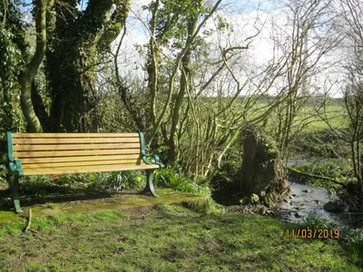 a park bench sitting next to a creek at 27 The Beeches, Gilcrux, Nr Cockermouth, Cumbria in Gilcrux