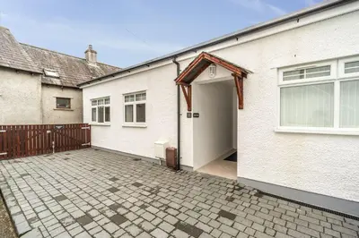 a white house with a door and a brick driveway at Sam's Cottage in Keswick