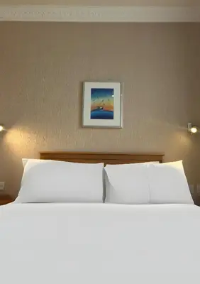 a bed with white pillows and a picture on the wall at Welbeck Hotel & Apartments IOM in Douglas