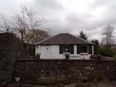 a small white house behind a stone wall at Groom's Cottage in Moffat