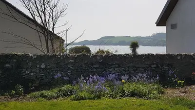 a stone retaining wall next to a house and flowers at 11 Laigh Isle in Isle of Whithorn