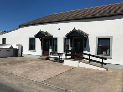 a white building with two benches in front of it at Dove cottage in Allonby