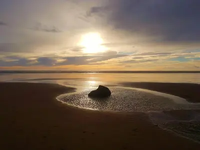 a rock in the sand on a beach with the sunset at OLD BAKEHOUSE in Holmrook