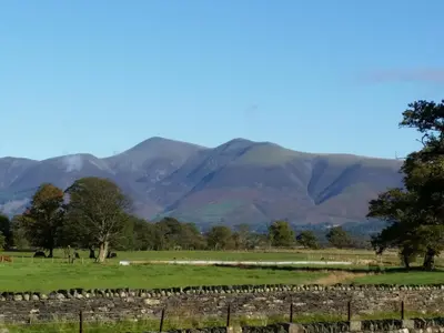 a field with a fence and mountains in the background at Field House Lodge in Borrowdale Valley