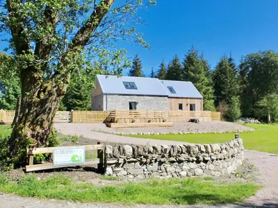 a log cabin with a stone wall and a tree at Ramerish Retreat in Laurieston