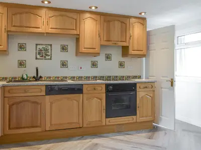a kitchen with wooden cabinets and a black dishwasher at Lorna's At The Grange - Uk11565 in Mockerkin