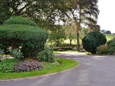 a garden with bushes and trees and a road at Lorna's At The Grange - Uk11565 in Mockerkin